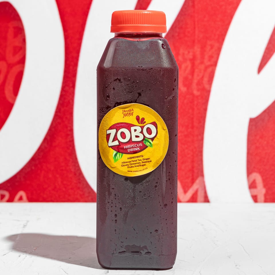 A bottle of Jamba Jollof Zobo Hibiscus Drink with condensation, against a red and white background.