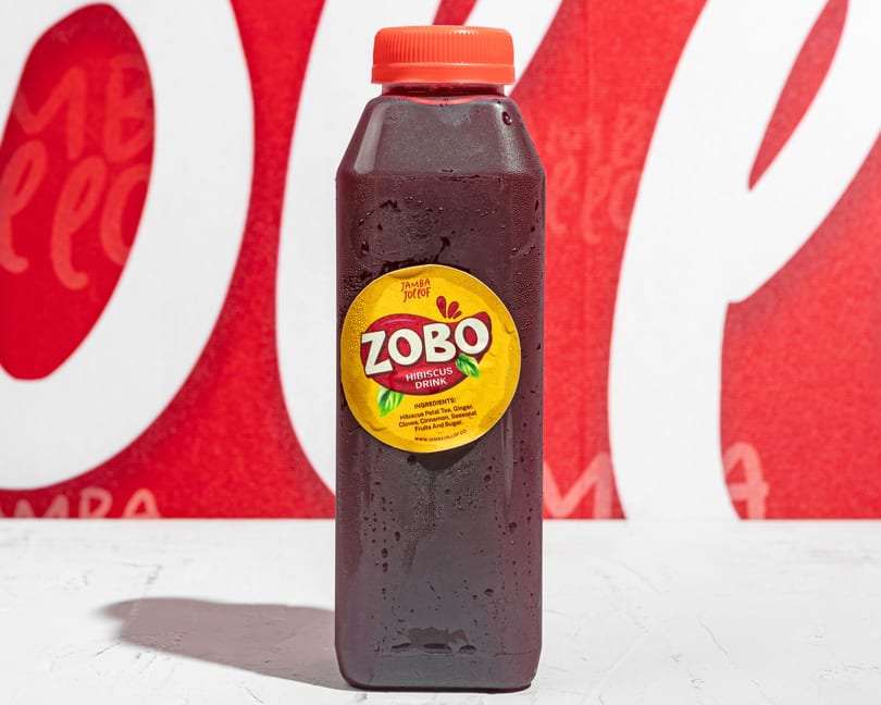 A bottle of Jamba Jollof Zobo Hibiscus Drink with condensation, against a red and white background.