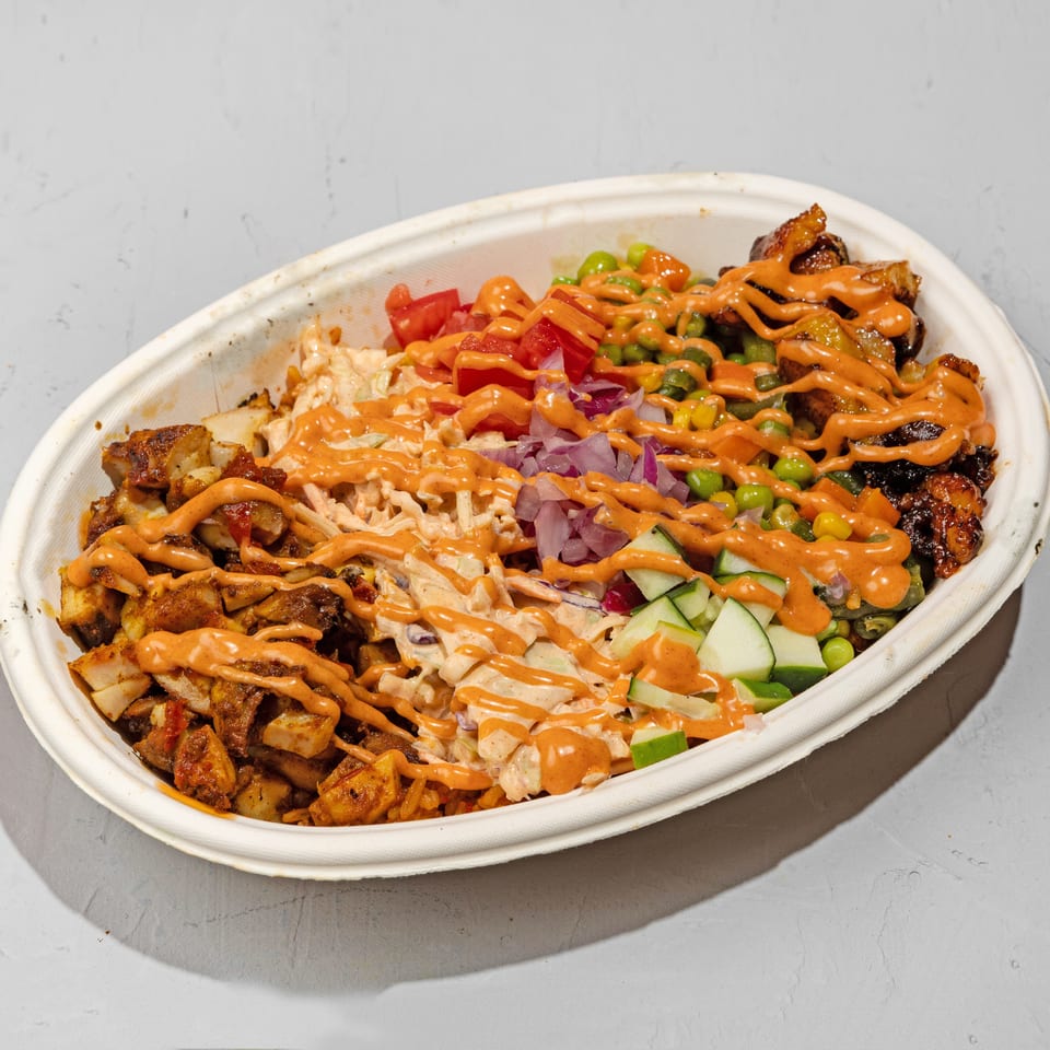 A large takeout bowl filled with various colorful ingredients, drizzled with orange sauce.