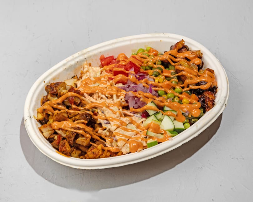 A large takeout bowl filled with various colorful ingredients, drizzled with orange sauce.