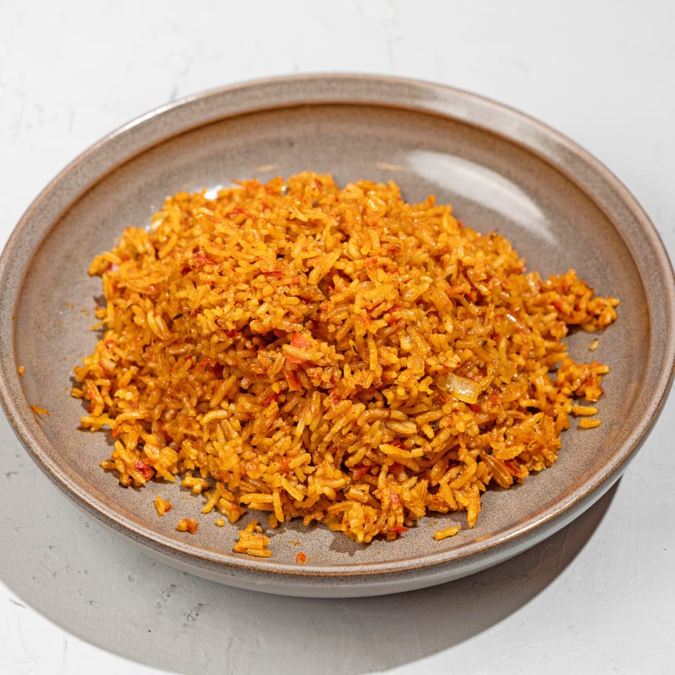 A large serving of vibrant orange jollof rice with red peppers in a rustic gray bowl.